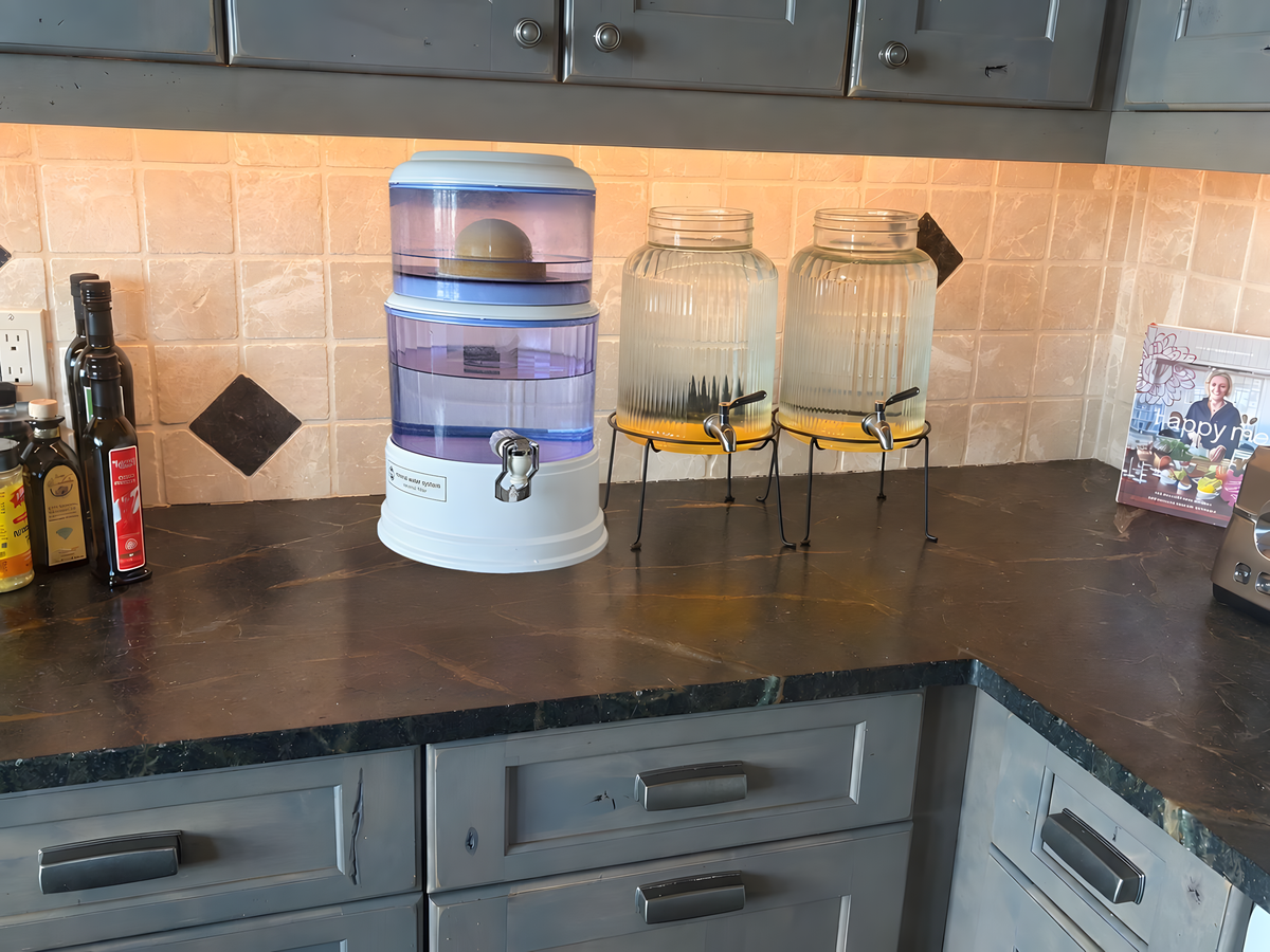 A ceramic gravity filter beside a line of six glass treatment jars on a kitchen counter